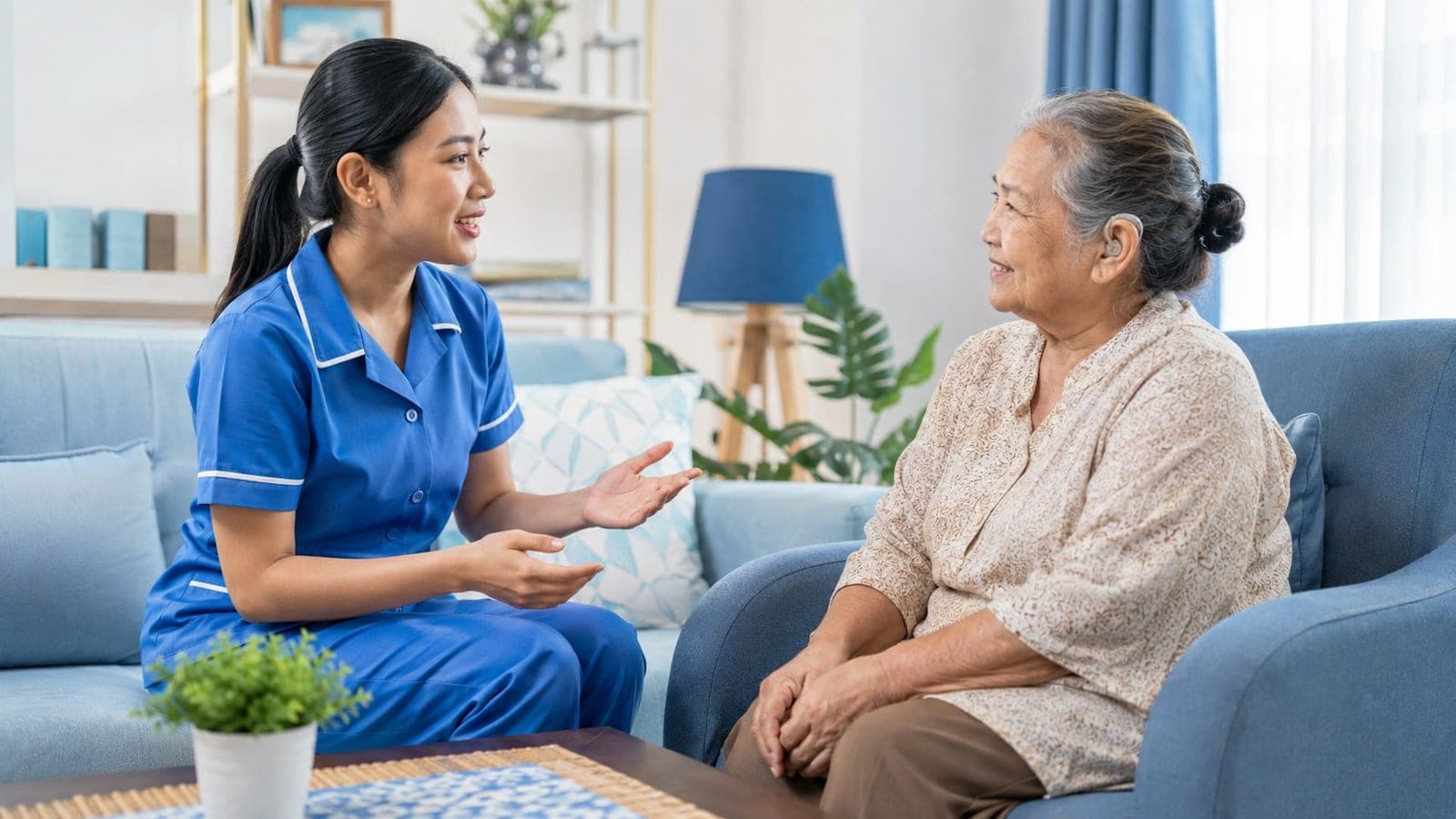 Caregiver STKI mengobrol hangat dengan seorang nenek di sofa ruang keluarga